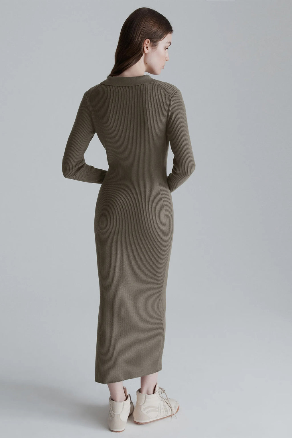 Woman wearing a long olive green ribbed dress on a plain background