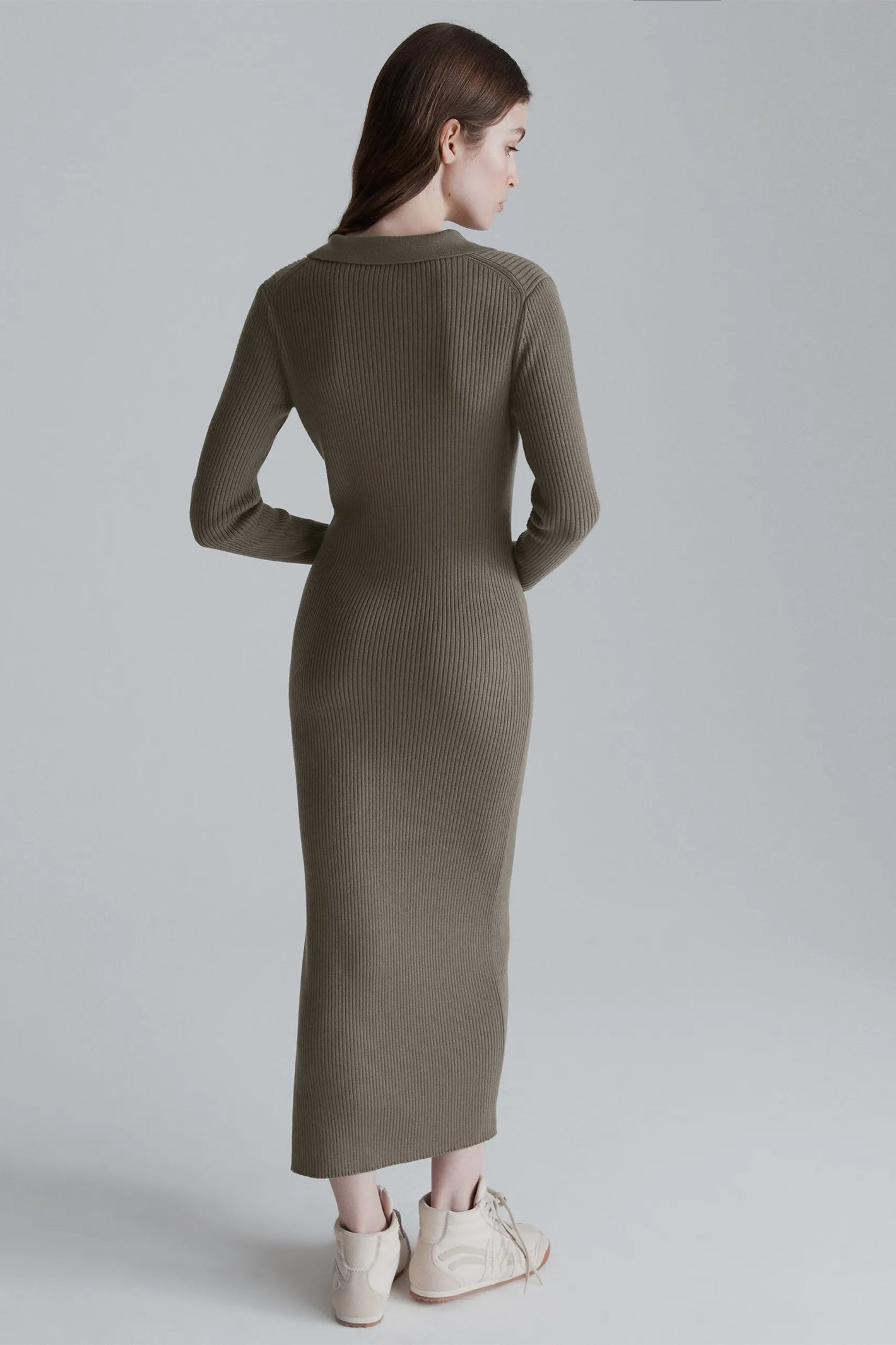 Woman wearing a long olive green ribbed dress on a plain background