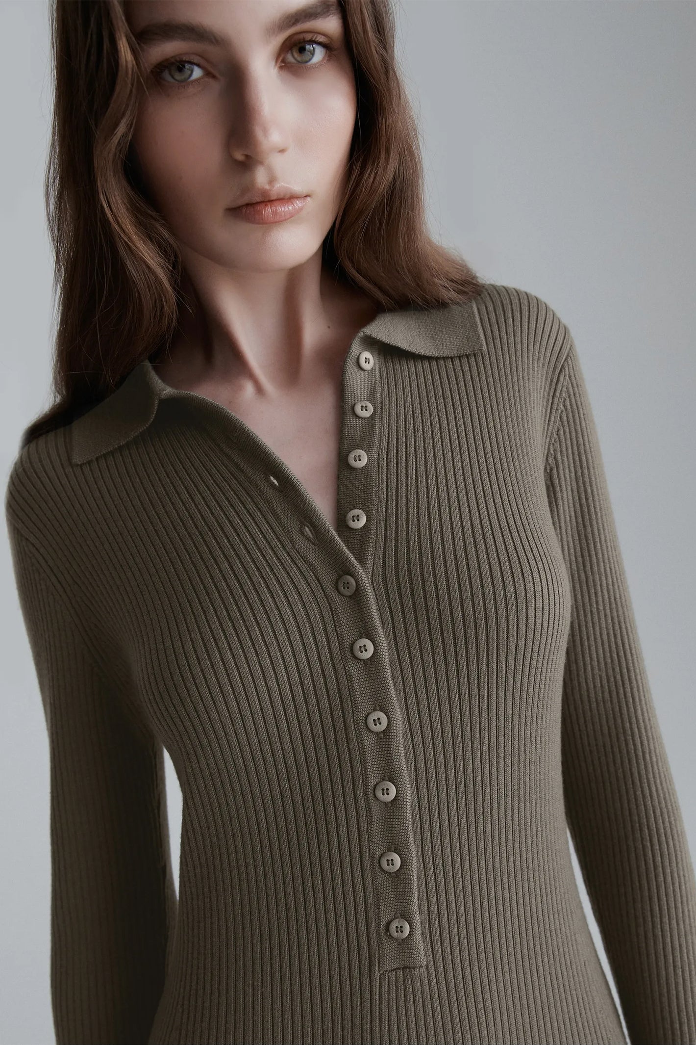 Woman wearing a brown ribbed sweater against a plain background