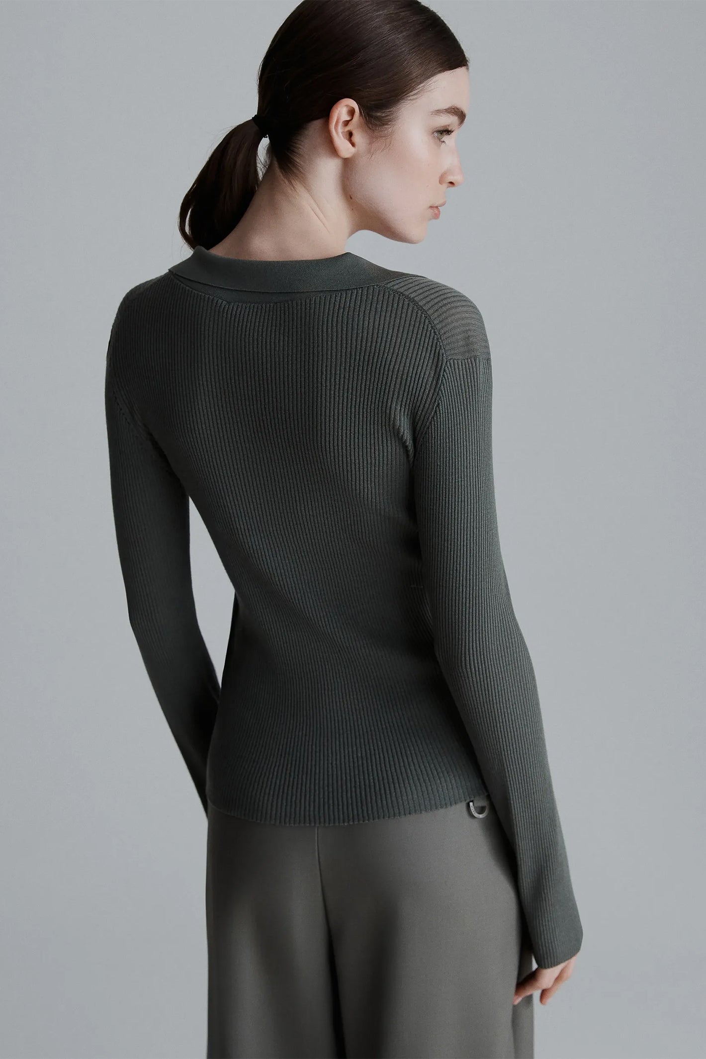 Woman wearing a dark green ribbed cardigan against a gray background