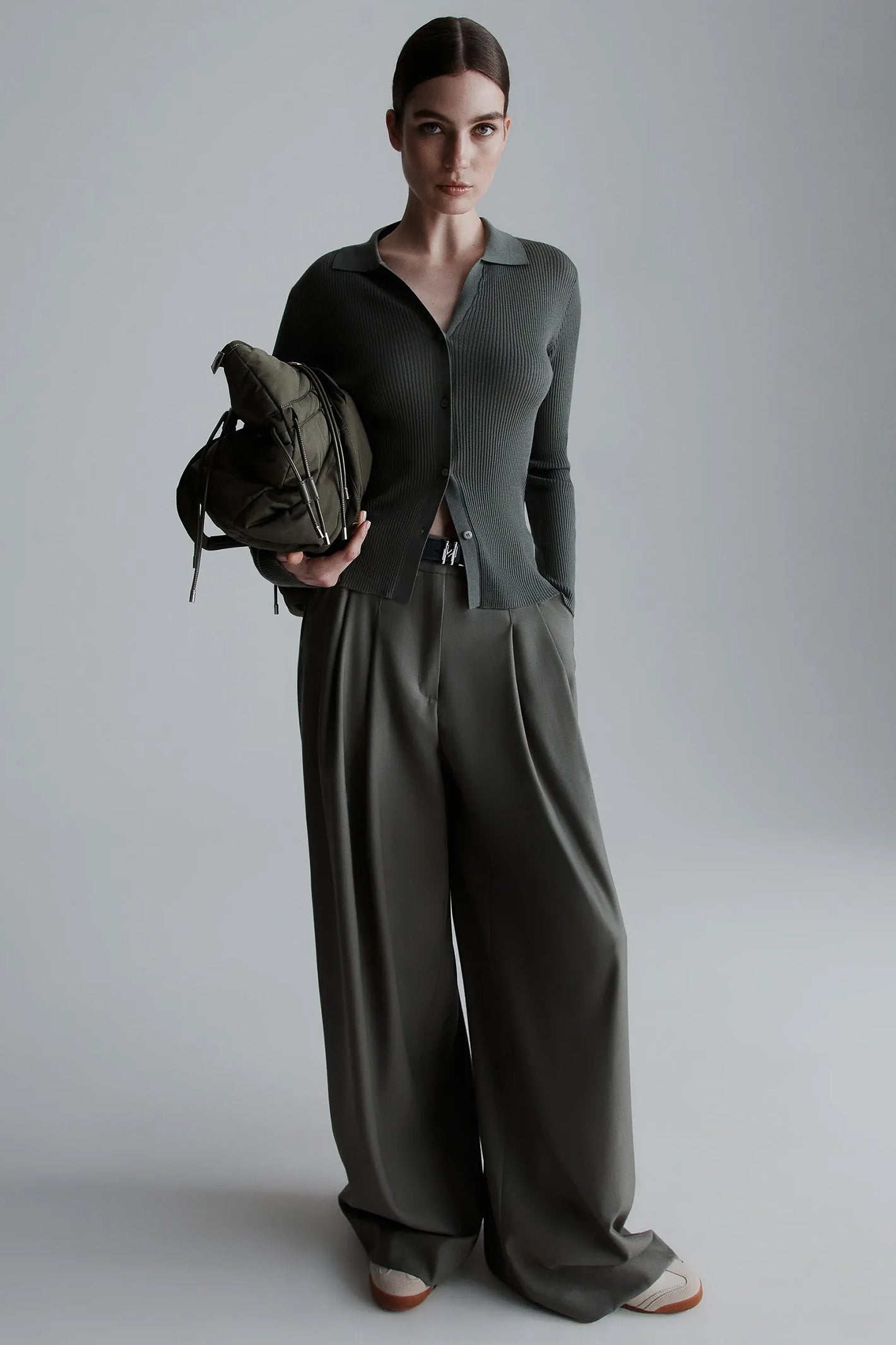 Person wearing a green cardigan holding a backpack against a plain background
