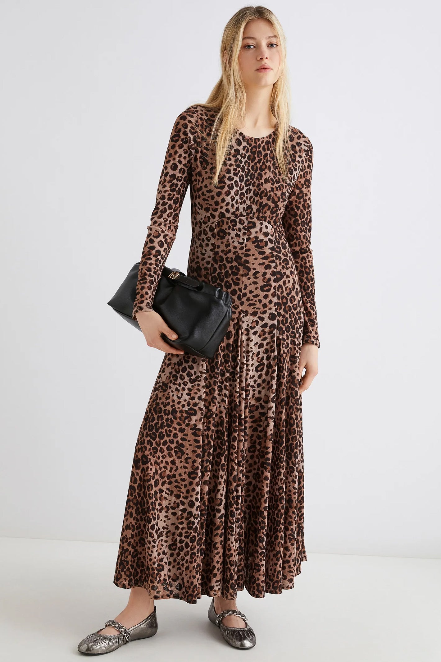 Woman wearing a leopard print dress holding a black clutch against a white background