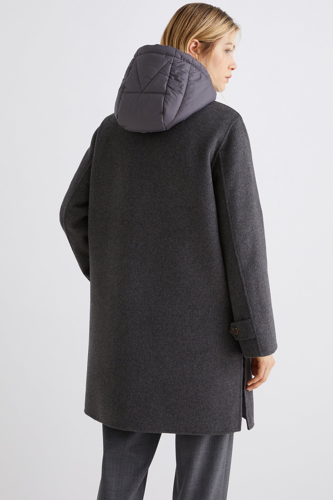 Person wearing a gray coat with a hood on a light gray background
