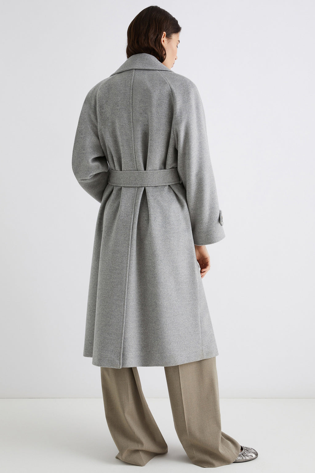 Person wearing a gray coat with a belt on a white background