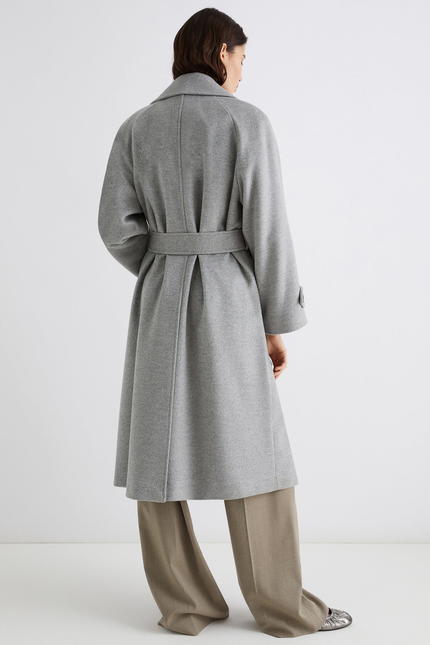 Person wearing a gray coat with a belt on a white background