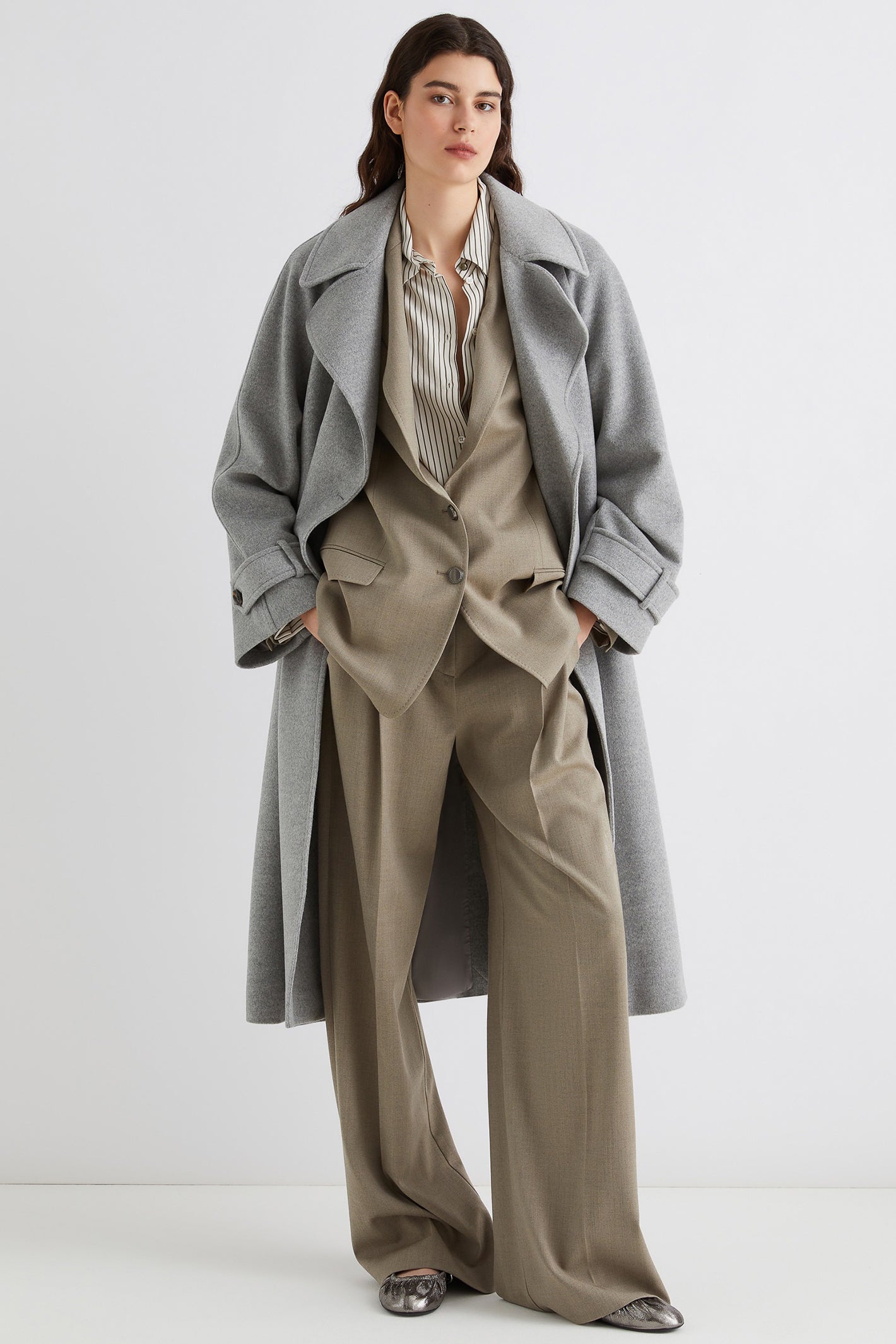 Woman wearing a gray coat over a beige suit on a white background