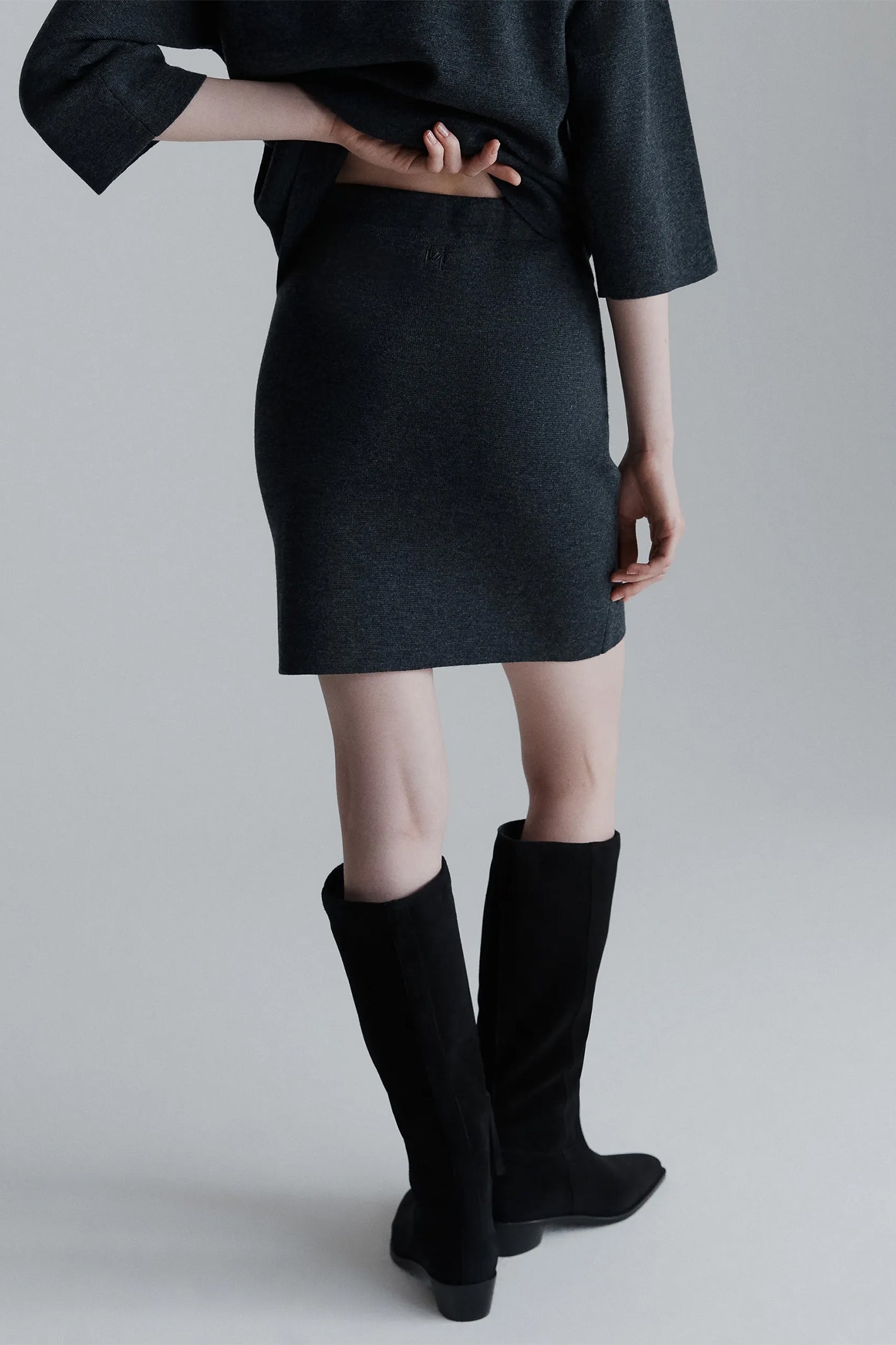 Person wearing a grey outfit with knee-high boots on a plain background