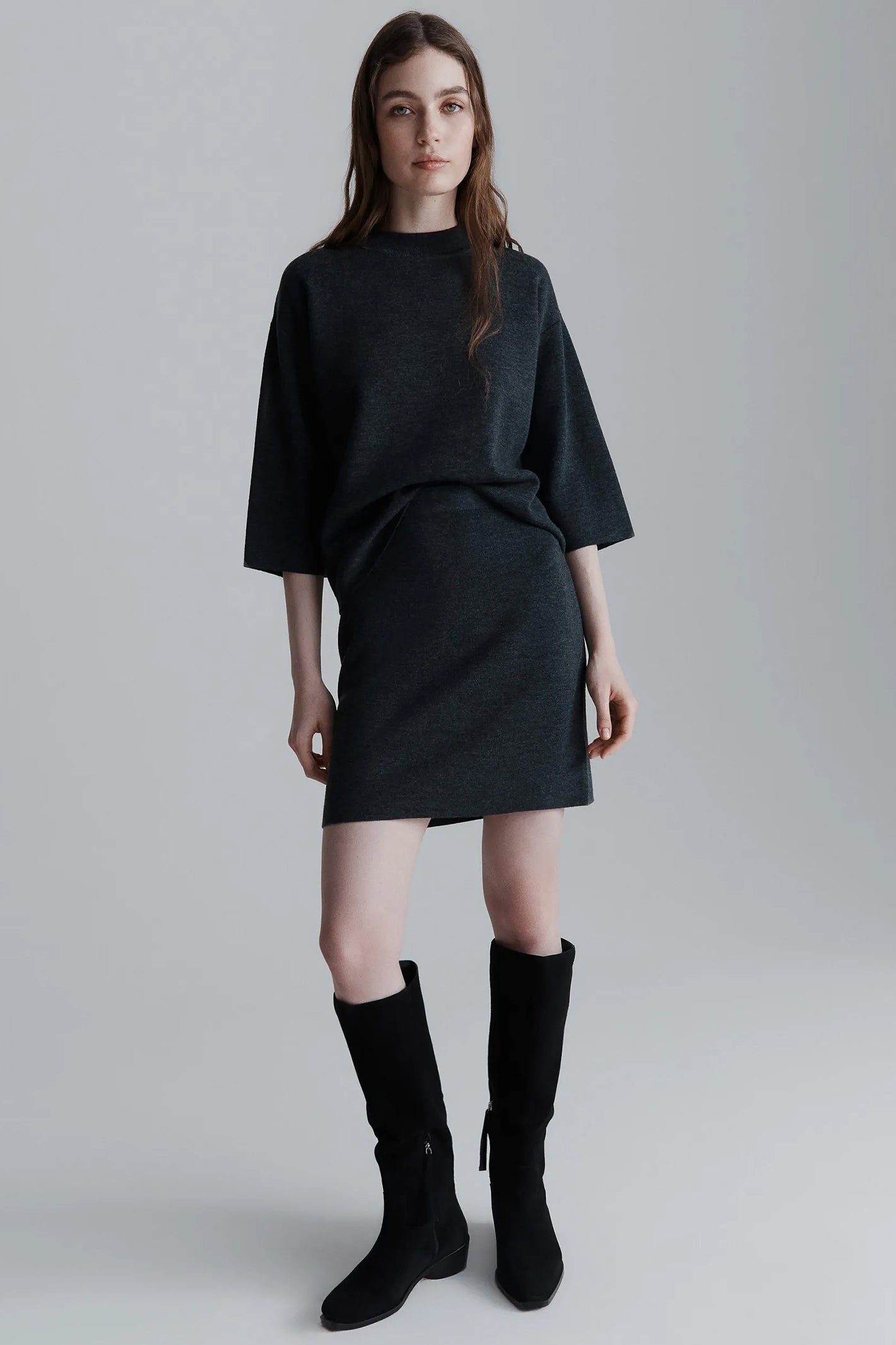 Woman wearing a grey outfit with knee-high boots on a plain background