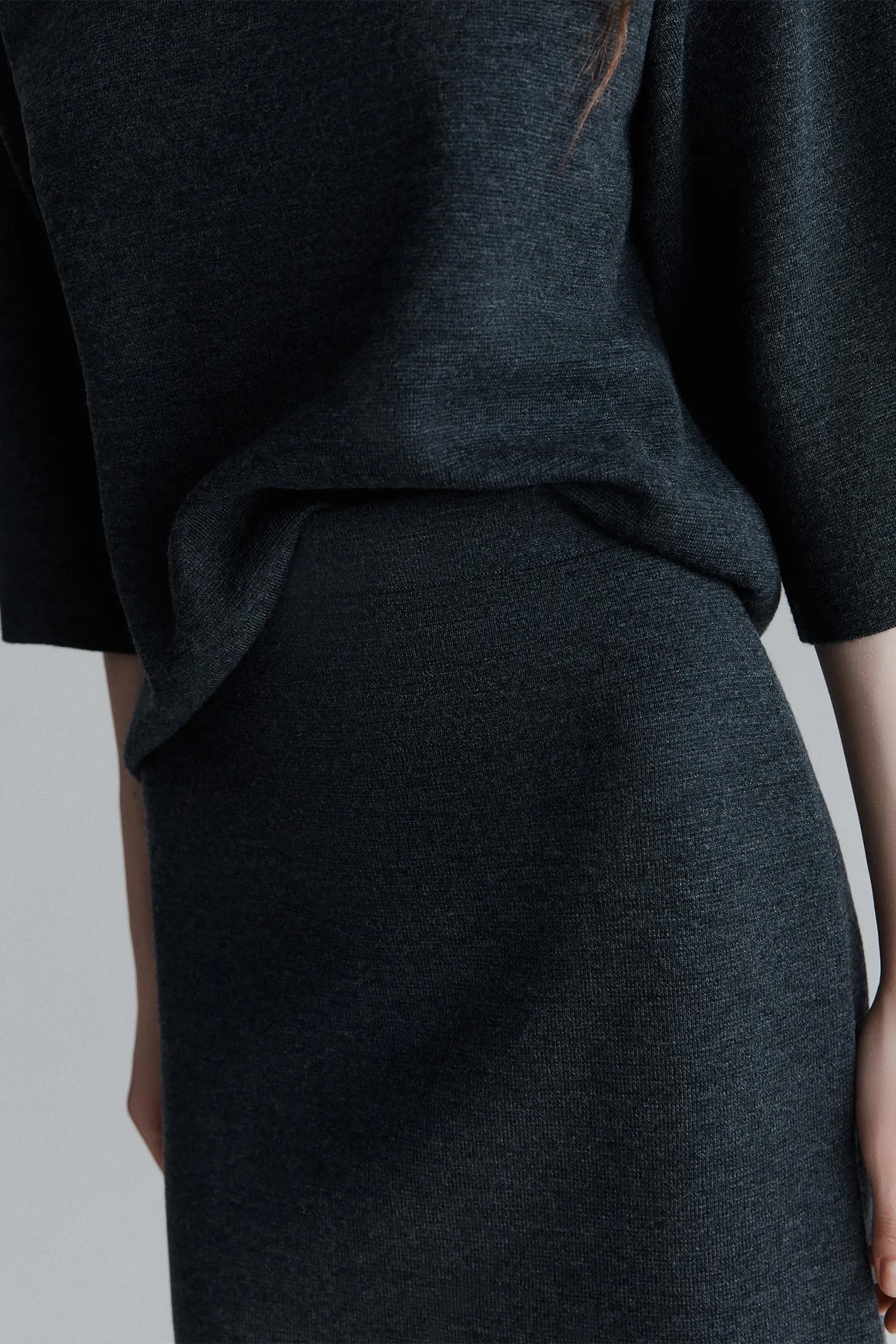 Person wearing a dark gray outfit with a plain background