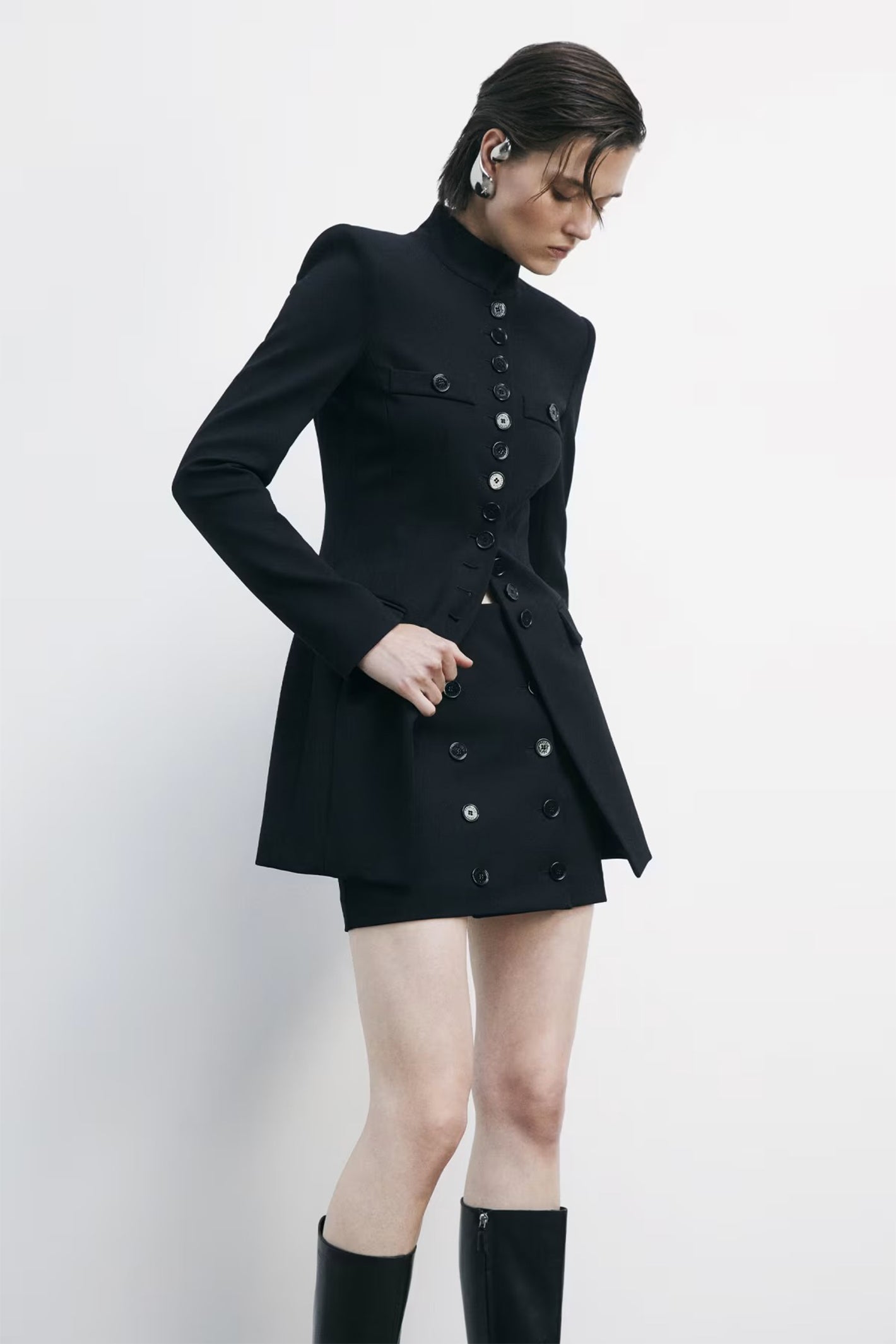 Person wearing a black coat and black knee-high boots on a white background