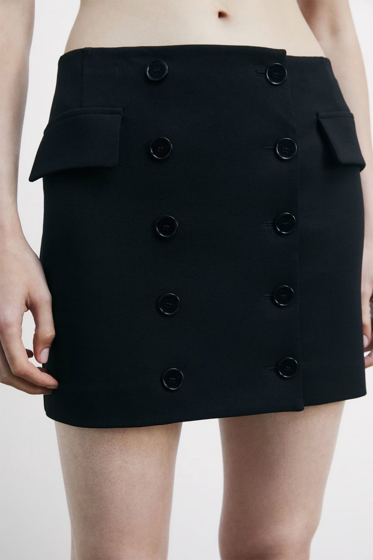 Black skirt with button details worn by a person on a white background