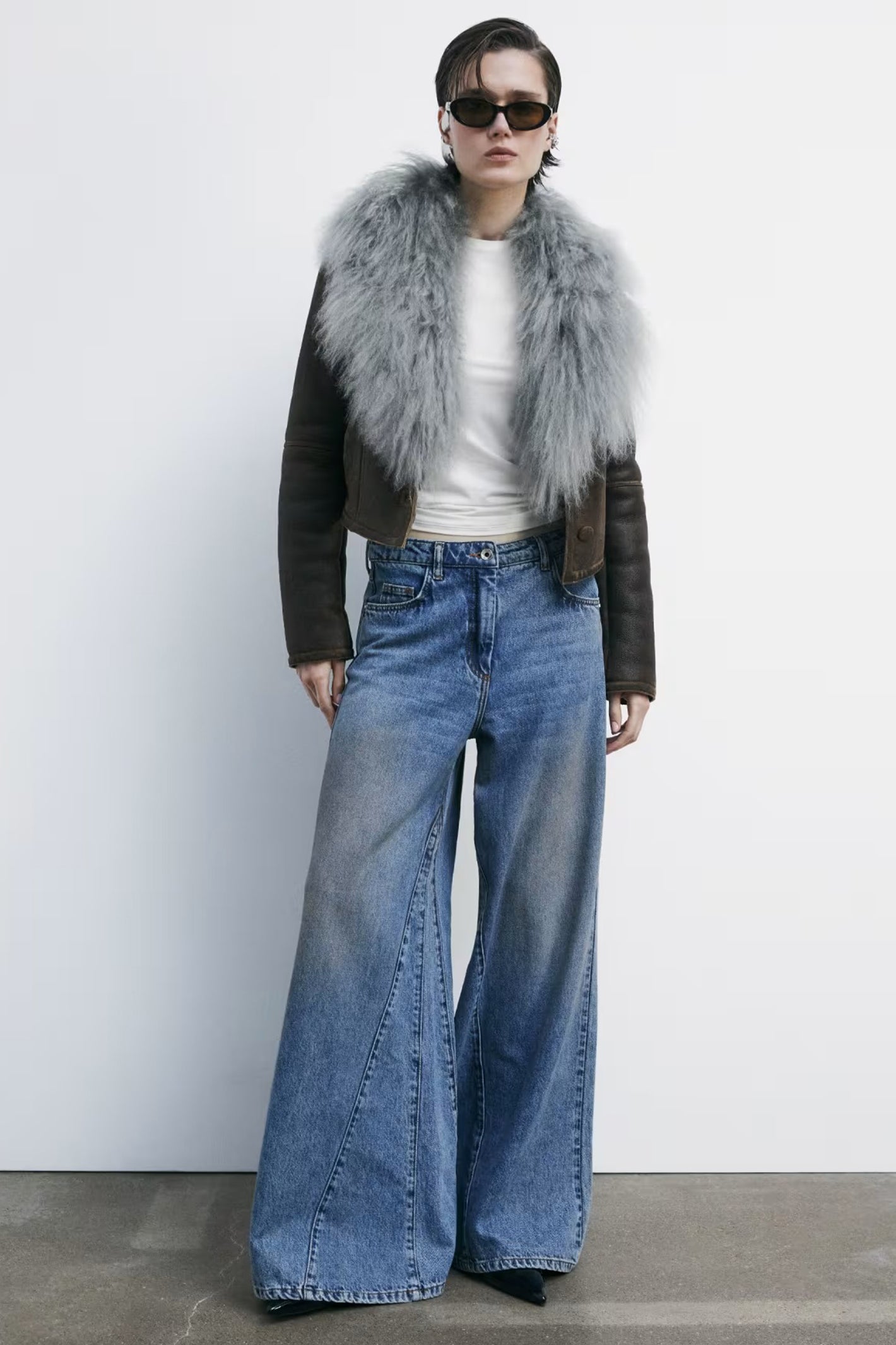 Person wearing a fur vest, white shirt, and blue jeans against a white background