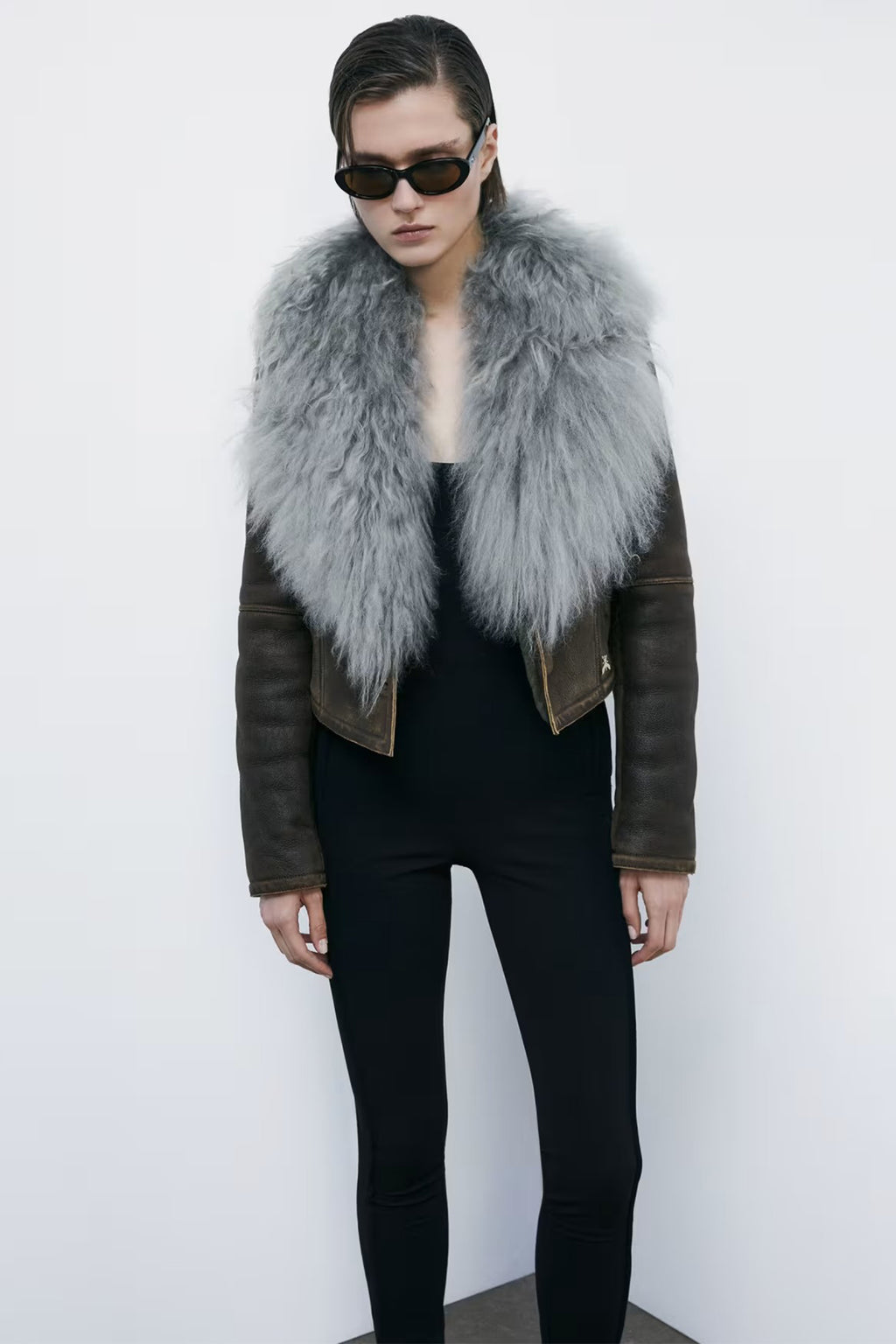 Person wearing a dark leather jacket with a gray fur vest against a white background