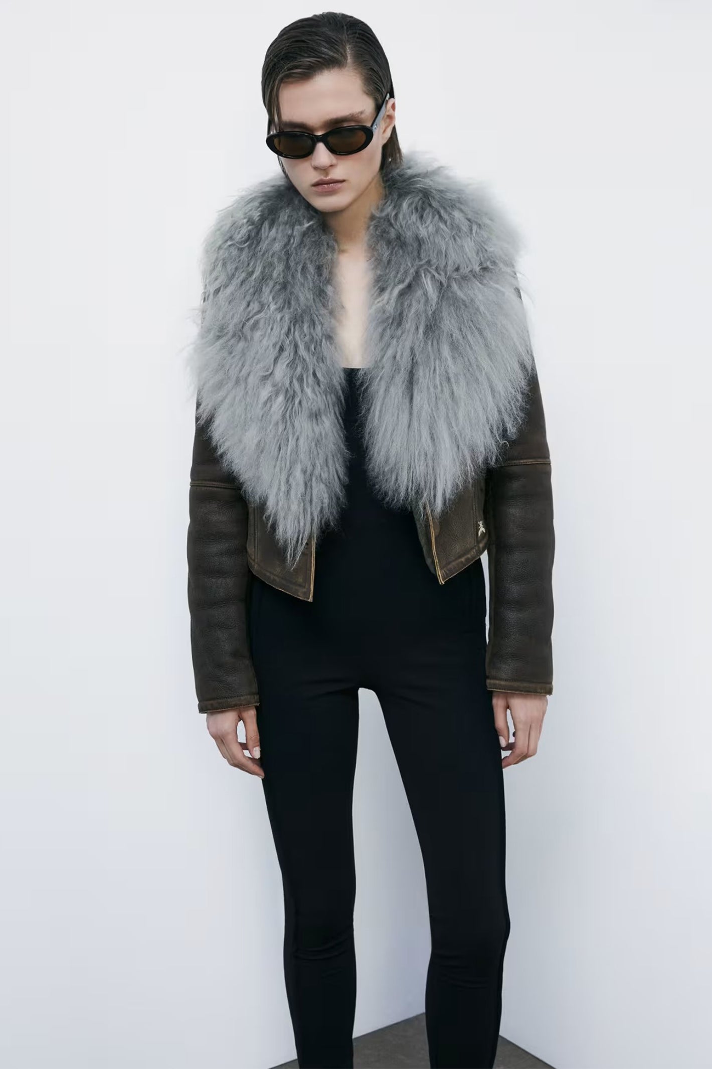 Person wearing a dark leather jacket with a gray fur vest against a white background