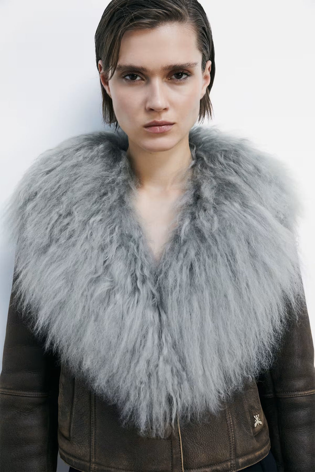 Person wearing a brown leather jacket with a gray fur collar against a white background