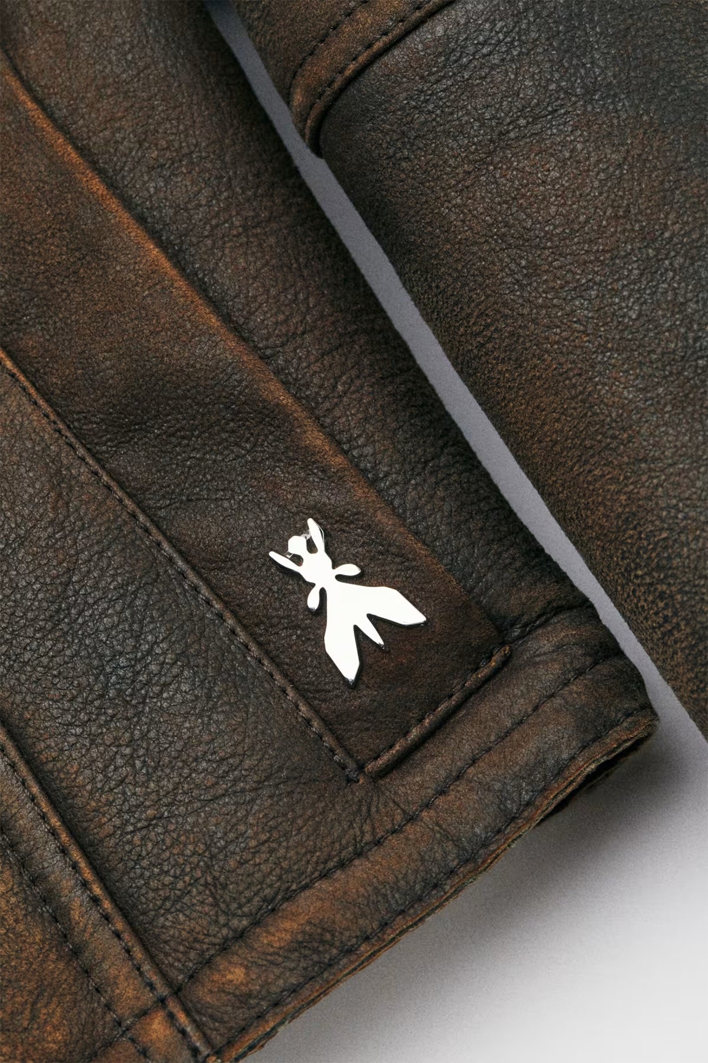 Close-up of a brown leather jacket with a white logo on a light gray background