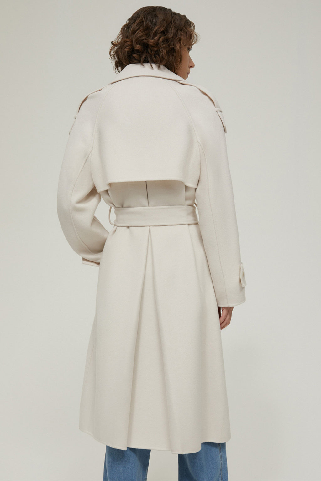 Person wearing a long cream coat on a plain background