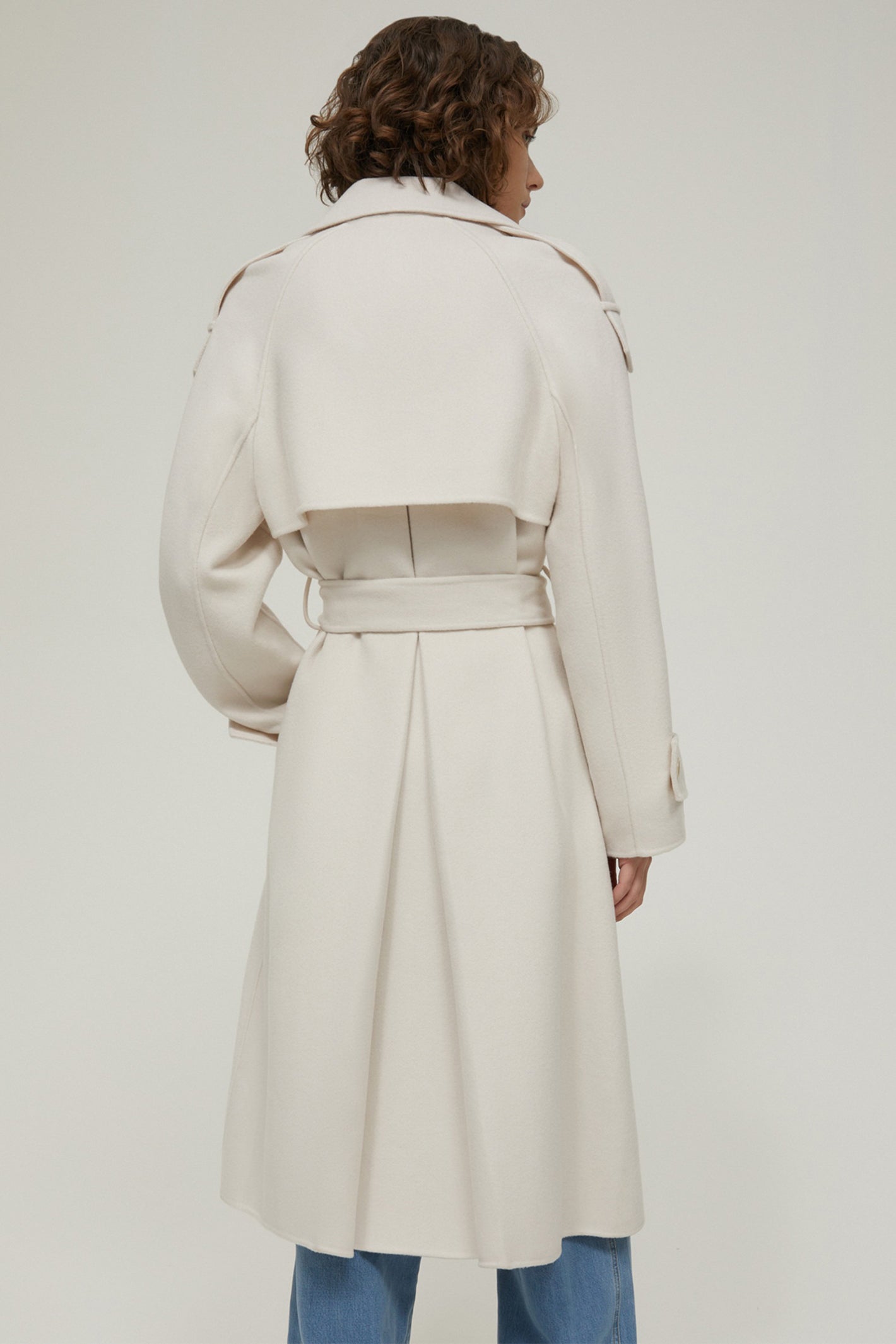 Person wearing a long cream coat on a plain background
