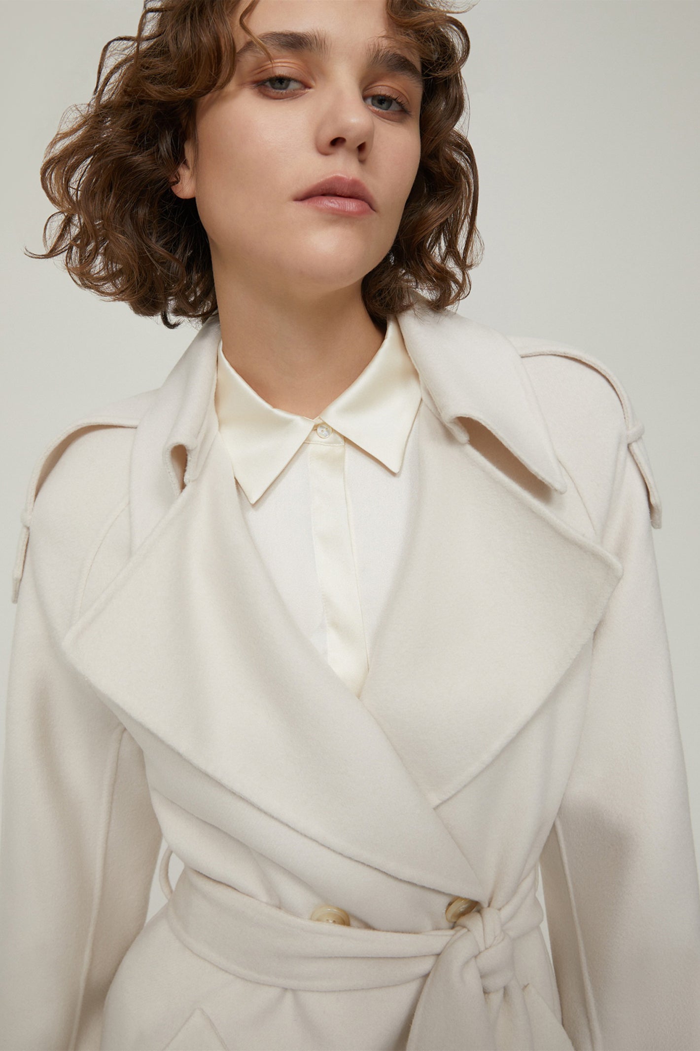 Person wearing a white coat with gold buttons on a plain background